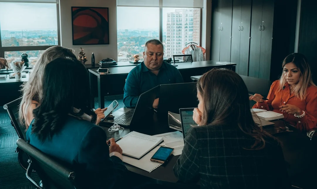 Two businesspeople review stock market data on a smartphone and laptop in a modern office environment.